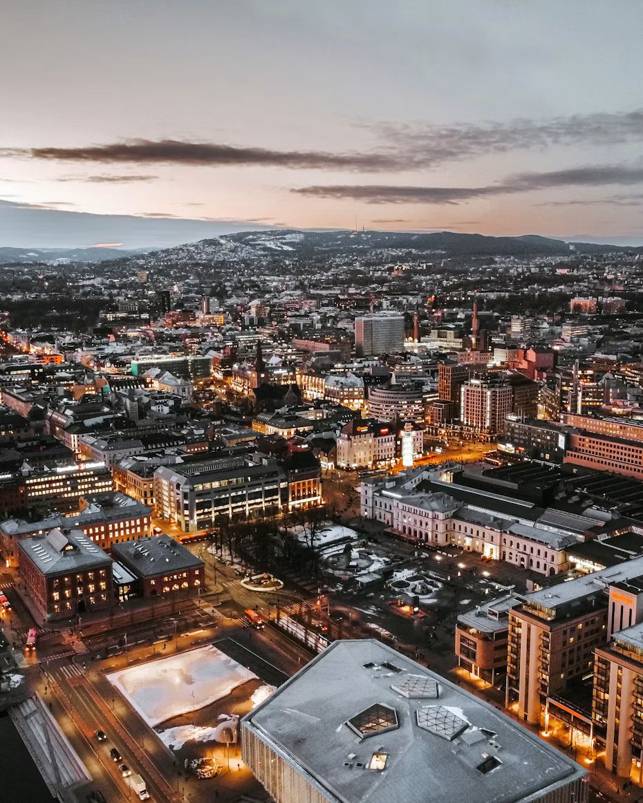 Oslo von oben in der Dämmerung, mit beleuchteten Häusern und Hügeln im Hintergrund