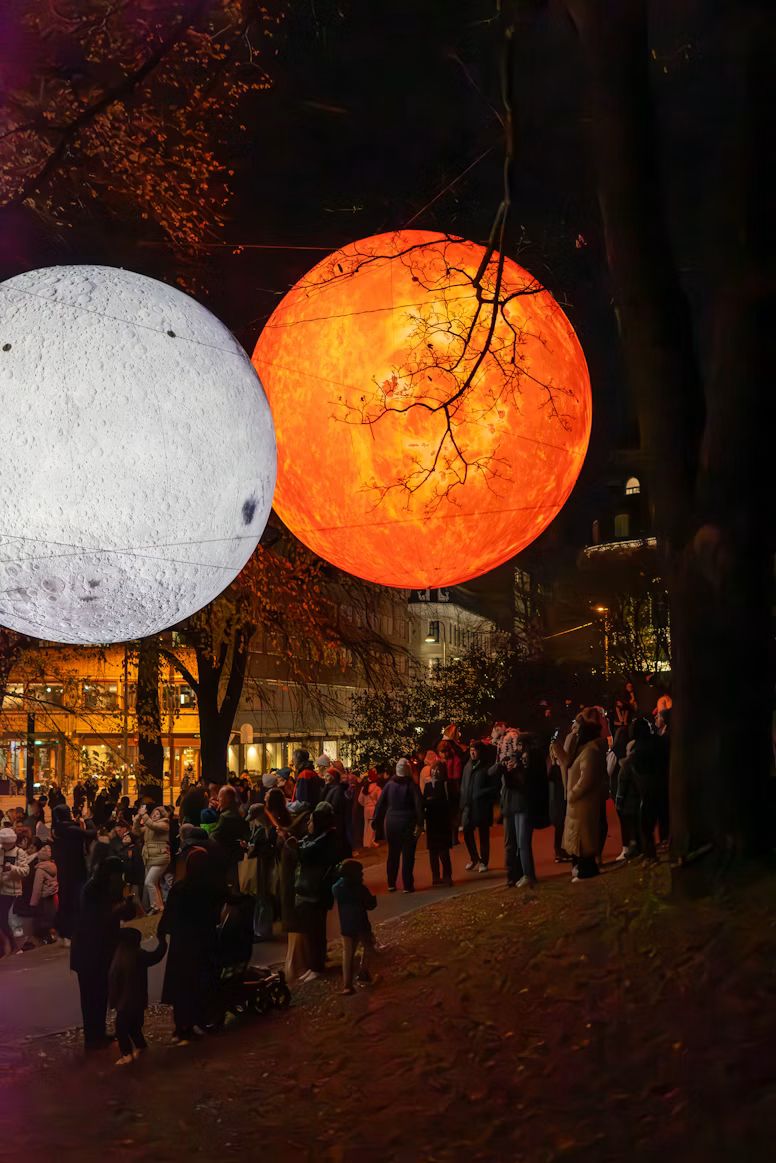 Große leuchtende Kugeln einer Lichtinstallation über Menschen am Abend
